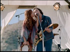 Riley Keough as Daisy Jones and Sam Claflin as Billy Dunne in Daisy Jones & The Six, singing into a shared microphone (Credit: Lacey Terrell/Prime Video)