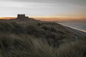 Children run through the sand dunes as the sun sets behind Bamburgh Castle