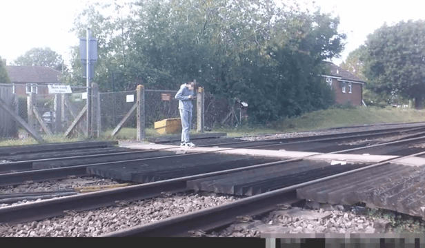 Teen stares at phone while stood on level crossing. Network Rail 