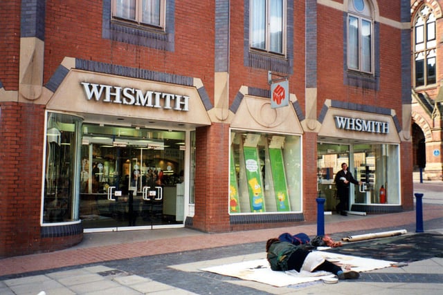 W. H. Smith on Lands Lane. A street artist is drawing on art work spread out over the ground outside. Albion Place can be seen on the right.