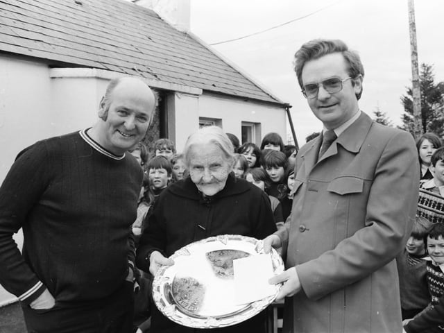 Mr. Pat Hughes, principal of Scoil Cholm Cille, Ballymena, Malin, presenting an inscribed silver salver to Mrs. Mary Collins of Beaugh, Malin, on the occasion of her 104th birthday in March 1981. On left is well-known musician Dinny McLaughlin, who organised a traditional session at Mary’s home.