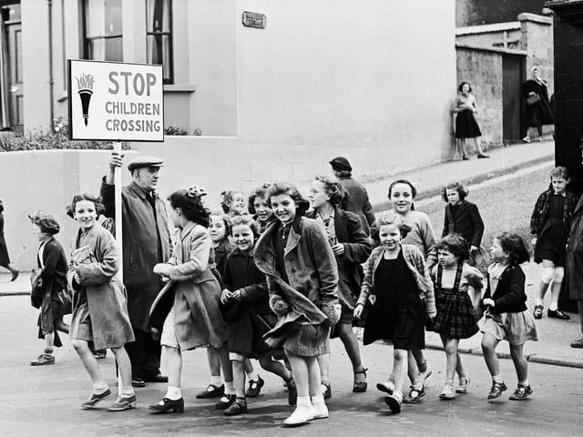 1953... Derry City Education Authority's new school patrol scheme comes into operation at Spencer Road. Here, patrolman L Bell ensures a traffic-free crossing for local schoolchildren at the busy junction with Malvern Terrace.