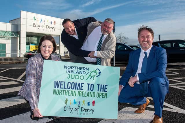 Pictured holding the welcome to the Northern Ireland Open sign are Steve Frazer, Managing Director of the City of Derry Airport, and Brenda Morgan, Head of Business Development. In the background Russell Brown, Chairman of the Northern Ireland Judo Federation demonstrates a technique on Mark Donald, Commercial Manager of the Federation.