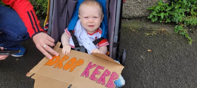 Little Ronan protesting for a drop kerb to be put in place to enable his parents to easily and safely push his pram across the road and into Brooke Park. The kerbs are currently very high on one side of the road and makes it difficult for people with prams or limited mobility to cross the road.