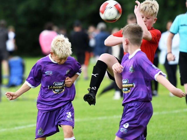 Altrincham F.C. under-12's player Sammy Neville makes a brave attempt to head the ball under pressure from a Newhill F.C. defender.