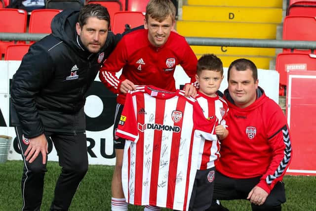 Derry City manager Ruaidhri Higgins and vice captain Ciaron Harkin present a signed Derry jersey to five year old Caleb Toland, who underwent major brain surgery last month, and his father Richie. Photographs by Kevin Moore