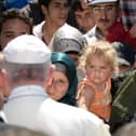 TOPSHOT - Pope Francis greets migrants and refugees at the Moria refugee camp on April 16, 2016 near the port of Mytilene, on the Greek island of Lesbos. Pope Francis received an emotional welcome today on the Greek island of Lesbos during a visit aimed at showing solidarity with migrants fleeing war and poverty.  Pope Francis, Orthodox Patriarch Bartholomew and Archbishop Jerome visit Lesbos today to turn the spotlight on Europe's controversial deal with Turkey to end an unprecedented refugee crisis.  AFP PHOTO POOL / FILIPPO MONTEFORTE (Photo by FILIPPO MONTEFORTE / POOL / AFP) (Photo by FILIPPO MONTEFORTE/POOL/AFP via Getty Images)