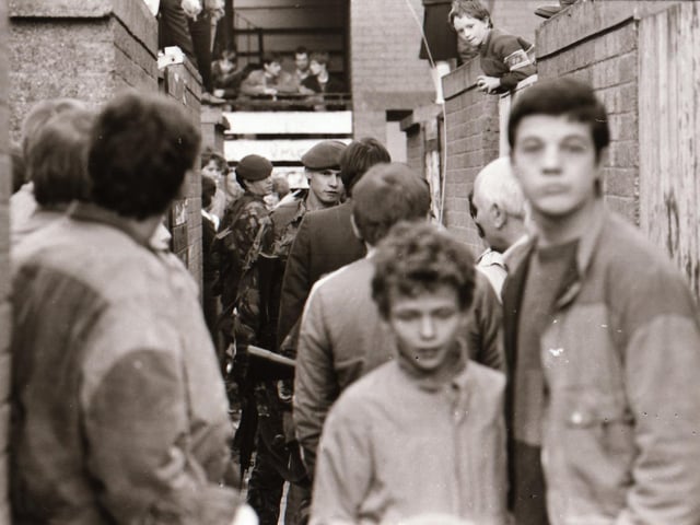 Neighbours and residents of Dove Gardens gather during a British army raid.