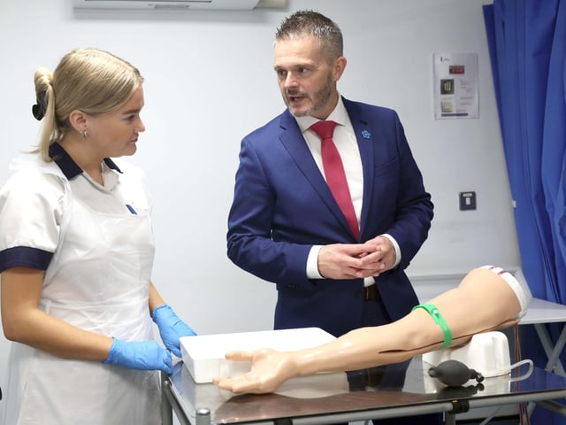 Bailey, a second-year adult nursing student at Ulster University, demonstrates how to take a blood sample using a simulated arm for Health Minister Robbie Butler during his visit to the School of Nursing and Paramedic Science at the Derry campus.