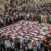 An elevated view shows mourners standing closely around rows of Palestinian flag-draped shrouds during a mass funeral amid rubble in Gaza City, Gaza Strip, on October 1, 2026. Gaza Civil Defense said the remains were among those of 105 people recovered from beneath the rubble of the Al-Taj residential complex and surrounding buildings in the Al-Yarmouk area, which were destroyed in Israeli strikes on October 25, 2023. The remains were taken for burial at Sheikh Radwan cemetery after the funeral. (Photo by Faiz Qreqa / Middle East Images / AFP via Getty Images)