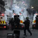 BALLYMENA, NORTHERN IRELAND - JUNE 10: PSNI officers stand behind armoured police vehicles as protesters throw projectiles and start fires on June 10, 2025 in Ballymena, Northern Ireland.  (Photo by Charles McQuillan/Getty Images)