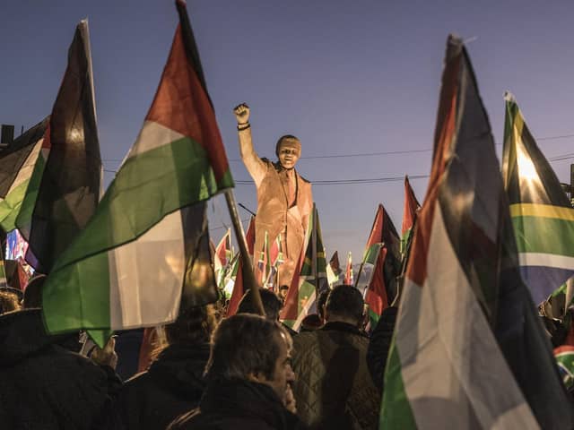 People raise flags and placards as they gather around a statue of late South African president Nelson Mandela to celebrate a landmark "genocide" case filed by South Africa against Israel at the International Court of Justice, in the occupied West Bank city of Ramallah on January 10, 2024. The ruling African National Congress (ANC) has long been a firm supporter of the Palestinian cause, often linking it to its own struggle against the white-minority government, which had cooperative relations with Israel. (Photo by MARCO LONGARI / AFP) (Photo by MARCO LONGARI/AFP via Getty Images)