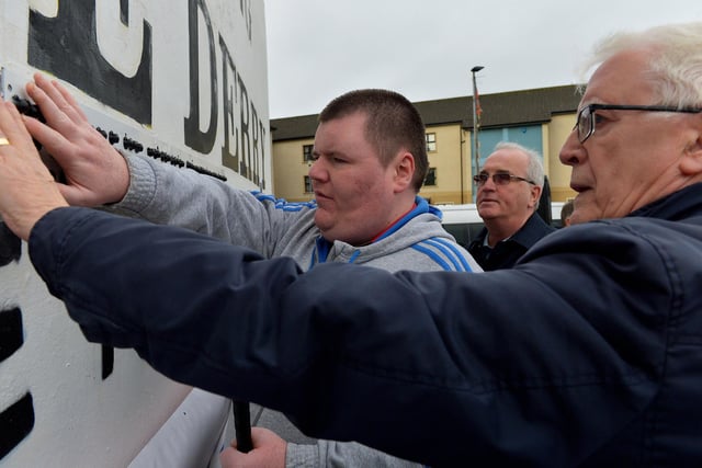 Brian from Tuned In reading the newly unveiled Braille sign on Free Derry Corner on Tuesday afternoon with John Kelly, Museum of Free Derry and   Richard Moore from Children in Crossfire. Photo: George Sweeney. DER2305GS – 64