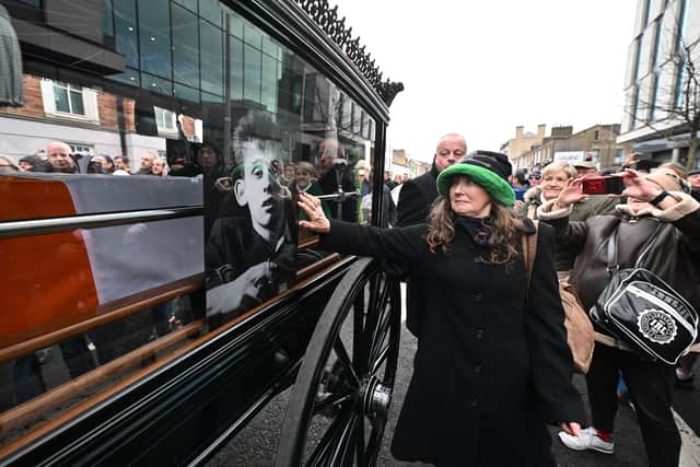 DUBLIN, IRELAND - DECEMBER 8: Members of the public touch the glass window of the carriage as the funeral procession of the late music singer Shane MacGowan takes place on December 8, 2023 in Dublin, Ireland. The public gathered on the streets of Dublin ahead of Shane MacGowan's funeral, set to take place on December 8. Born on Christmas Day in Pembury, Kent, in 1957, he's best known as the lead singer and songwriter of the Pogues. Raised in Tunbridge Wells by Irish parents, MacGowan changed up Irish folk music by infusing punk style and attitude, as showcased in the popular 1988 Christmas ballad "Fairytale of New York." He is survived by his wife, Victoria Mary Clarke, sister Siobhan, and father. (Footage by Charles McQuillan/Getty Images)