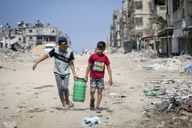 Children carry water as they walk past buildings destroyed during Israeli bombardment in Khan Yunis, on the southern Gaza Strip on April 16, 2024, as fighting continues between Israel and the Palestinian militant group Hamas. (Photo by AFP) (Photo by -/AFP via Getty Images)