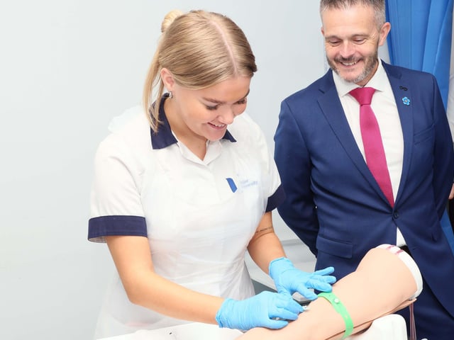 Bailey, a second-year adult nursing student at Ulster University, demonstrates how to take a blood sample using a simulated arm for Health Minister Robbie Butler during his visit to the School of Nursing and Paramedic Science at the Derry campus.