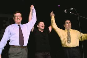 Irish rock band U2's lead singer Bono (C) holds up the arms of Ulster Unionist leader David Trimble (L) and SDLP leader John Hume on stage during a concert given by U2 and Ash at the Waterfront concert hall to promote the yes vote for Friday's peace referendum. Photo credit: GERRY PENNY/AFP via Getty Images