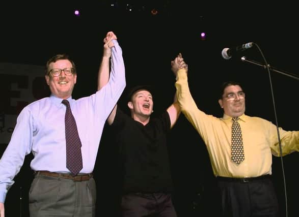 Irish rock band U2's lead singer Bono (C) holds up the arms of Ulster Unionist leader David Trimble (L) and SDLP leader John Hume on stage during a concert given by U2 and Ash at the Waterfront concert hall to promote the yes vote for Friday's peace referendum. Photo credit: GERRY PENNY/AFP via Getty Images