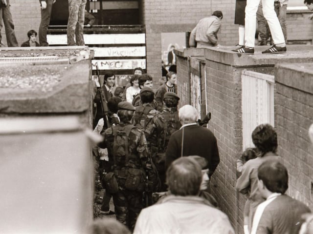 Neighbours and residents of Dove Gardens gather during a British army raid.