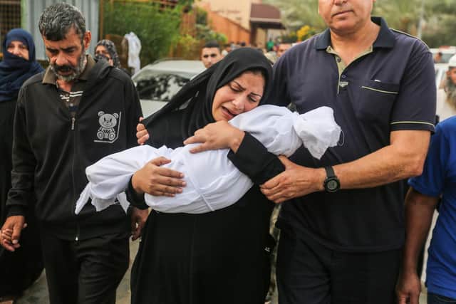 KHAN YUNIS, GAZA A woman cradles her son, eight-month-old Muhammad Bilal Abu Salah, as residents collect the bodies of Palestinians killed in reported Israeli air strikes on October 28, 2023 in Khan Yunis, Gaza. (Photo by Ahmad Hasaballah/Getty Images)