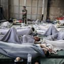 A member of the Coastguard overlooks suvivors as they rest in a warehouse used as a temporary shelter, after a boat carrying dozens of migrants sank in the Ionian Sea, in Kalamata town, Greece, on June 14, 2023. (Photo by Menelaos Myrillas / SOOC / SOOC via AFP) (Photo by MENELAOS MYRILLAS/SOOC/AFP via Getty Images)