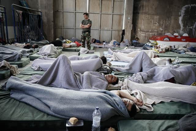 A member of the Coastguard overlooks suvivors as they rest in a warehouse used as a temporary shelter, after a boat carrying dozens of migrants sank in the Ionian Sea, in Kalamata town, Greece, on June 14, 2023. (Photo by Menelaos Myrillas / SOOC / SOOC via AFP) (Photo by MENELAOS MYRILLAS/SOOC/AFP via Getty Images)