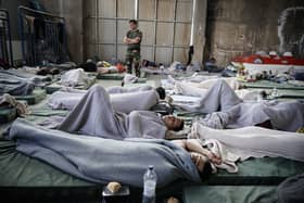 A member of the Coastguard overlooks suvivors as they rest in a warehouse used as a temporary shelter, after a boat carrying dozens of migrants sank in the Ionian Sea, in Kalamata town, Greece, on June 14, 2023. (Photo by Menelaos Myrillas / SOOC / SOOC via AFP) (Photo by MENELAOS MYRILLAS/SOOC/AFP via Getty Images)