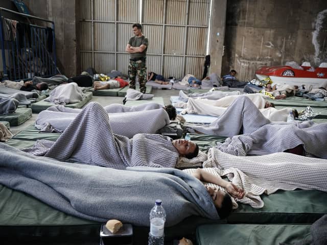 A member of the Coastguard overlooks suvivors as they rest in a warehouse used as a temporary shelter, after a boat carrying dozens of migrants sank in the Ionian Sea, in Kalamata town, Greece, on June 14, 2023. (Photo by Menelaos Myrillas / SOOC / SOOC via AFP) (Photo by MENELAOS MYRILLAS/SOOC/AFP via Getty Images)