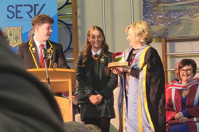 Secretary Hillary Clinton accepting a model of the joint schools badge from Head Girl of St Mary's and Head Boy of Limavady High School.