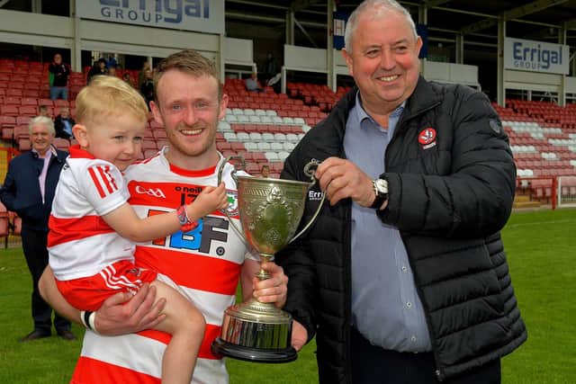 Derry County chairman John Keenan presents the Neil Carlin Cup to Ballerin captain Paul Ferris, after their victory over Doire Trasna in Celtic Park, on Sunday afternoon. Also in the photo is Paul’s son, Darragh. Photo: George Sweeney. DER23119GS – 09