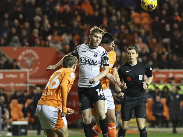 Morecambe's Jacob Davenport heads the ball clear under pressure from Blackpool's Luke Mariette.