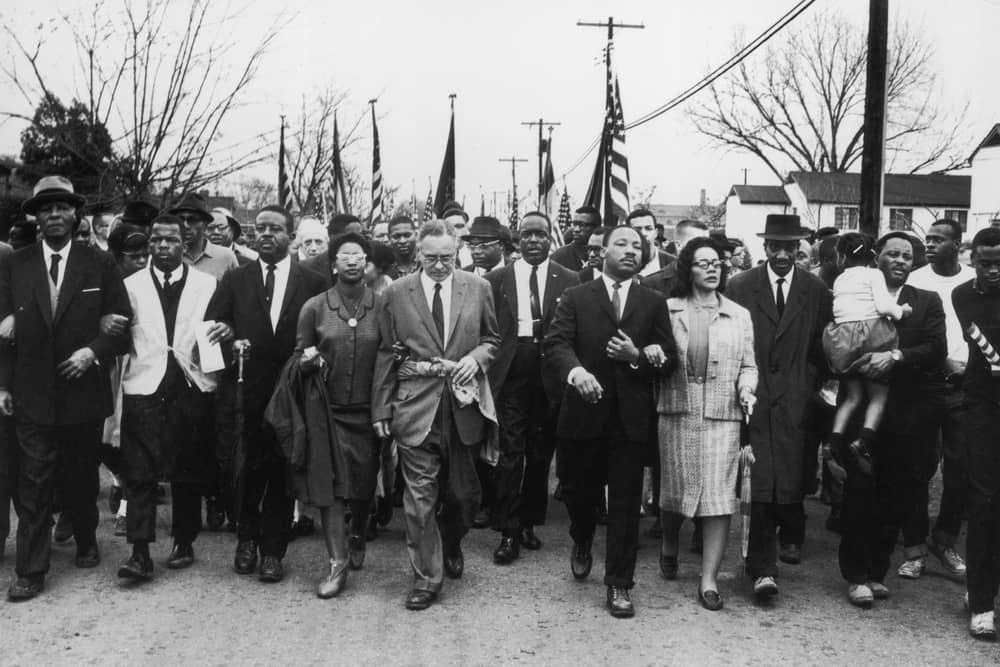 March 1965:  American civil rights campaigner Martin Luther King (1929  - 1968) and his wife Coretta Scott King lead a black voting rights march from Selma, Alabama, to the state capital in Montgomery;  among those pictured are, front row, politician and civil rights activist John Lewis (1940 – 2020), Reverend Ralph Abernathy (1926 - 1990), Ruth Harris Bunche (1906 - 1988), Nobel Prize-winning political scientist and diplomat Ralph Bunche (1904 - 1971), activist Hosea Williams (1926 – 2000 right carrying child). (Photo by William Lovelace/Daily Express/Hulton Archive/Getty Images)