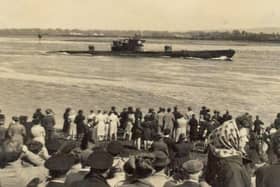 A crowd watches from the shore as a submarine makes its way along the Foyle
