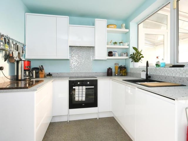 The kitchen from another angle, showing its range of matching wall and base units, with work surfaces, and a one-and-a-half sink and drainer with mixer tap. The flooring is fitted vinyl, and a door leads to the back of the property.