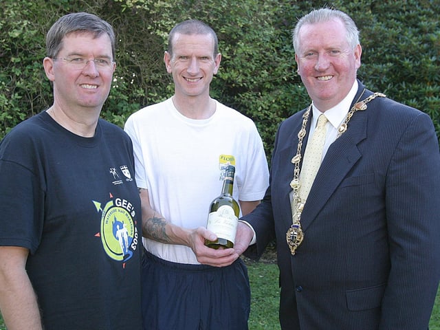 The Mayor of Derry Councillor Shane Gallagher, presents a prize to Billy Orr, the first Waterside runner to complete the Waterside half-marathon.  Included is Eamon Gee, proprietor of Gee's supermarket, co-sponsors of the race.  (1609T58).:.