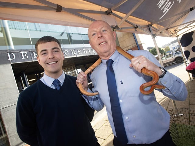 Derry CU staffers John Sheerin and Michael Gallagher pictured posing with a snake during Saturday's International Credit Union Day. : .