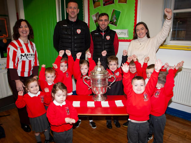 Nursery pupils at St. Eugene’s PS show their support for Derry City on Monday last as players Shane McEleney and Joe Thompson brought the FAI Cup to the school.