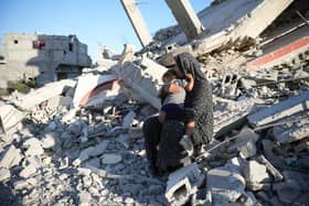 Aaliyah* sits on the remains of a damaged building with her daughter in their neighbourhood in southern Gaza, in October 2024. The mother of six built a temporary shelter opposite her house after it was demolished in airstrikes in February 2024. Her daughter insists on staying near the site of their former home and cries if they venture further out. Aaliyah depends entirely on aid to feed her family as she has been unable to earn an income since October 2023. Photo: DEC/Arete/Abdallah Alsayed  *Name changed to protect identity  Quotes from Aaliyah, October 2024:  “My family consists of eight members - me, my husband, five daughters, and a son.   I had a house that was demolished in February.  We live in a tent near the rubble of our home. I always find my daughter sitting by the rubble, crying, and she only calms down when she sits there.  We had shelter and a roof over our heads. Now, we have nothing but a piece of fabric that doesn't even protect us from the rain.  My daughter is the main reason we live near the rubble of our house. She only stops crying and calms down when she sits there.  We are suffering a lot, especially in winter. We have nothing to protect us from the rain or a shelter like other people, and my little daughter freezes from the cold.”