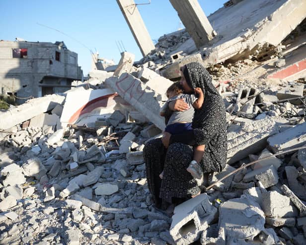 Aaliyah* sits on the remains of a damaged building with her daughter in their neighbourhood in southern Gaza, in October 2024. The mother of six built a temporary shelter opposite her house after it was demolished in airstrikes in February 2024. Her daughter insists on staying near the site of their former home and cries if they venture further out. Aaliyah depends entirely on aid to feed her family as she has been unable to earn an income since October 2023. Photo: DEC/Arete/Abdallah Alsayed  *Name changed to protect identity  Quotes from Aaliyah, October 2024:  “My family consists of eight members - me, my husband, five daughters, and a son.   I had a house that was demolished in February.  We live in a tent near the rubble of our home. I always find my daughter sitting by the rubble, crying, and she only calms down when she sits there.  We had shelter and a roof over our heads. Now, we have nothing but a piece of fabric that doesn't even protect us from the rain.  My daughter is the main reason we live near the rubble of our house. She only stops crying and calms down when she sits there.  We are suffering a lot, especially in winter. We have nothing to protect us from the rain or a shelter like other people, and my little daughter freezes from the cold.”