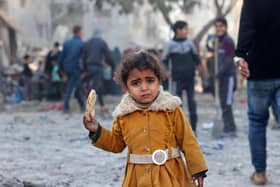 A Palestinian girl eats a piece of bread as people check debris on February 22, 2024, following overnight Israeli air strikes in Rafah refugee camp in the southern Gaza Strip, as battles between Israel and the Palestinian militant group Hamas continue. (Photo by MOHAMMED ABED / AFP) (Photo by MOHAMMED ABED/AFP via Getty Images)