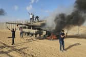 Palestinians celebrate by a destroyed Israeli tank at the Gaza Strip fence east of Khan Younis Saturday, Oct. 7, 2023. The militant Hamas rulers of the Gaza Strip carried out an unprecedented, multi-front attack on Israel at daybreak Saturday, firing thousands of rockets as dozens of Hamas fighters infiltrated the heavily fortified border in several locations by air, land, and sea and catching the country off-guard on a major holiday (AP Photo/Hassan Eslaiah)