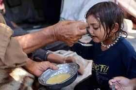 A Palestinian man feeds lentil soup to a child in the Daraj neighbourhood in Gaza City on August 3, 2025. (Photo by Omar AL-QATTAA / AFP) (Photo by OMAR AL-QATTAA/AFP via Getty Images).