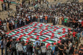 An elevated view shows mourners standing closely around rows of Palestinian flag-draped shrouds during a mass funeral amid rubble in Gaza City, Gaza Strip, on October 1, 2026. Gaza Civil Defense said the remains were among those of 105 people recovered from beneath the rubble of the Al-Taj residential complex and surrounding buildings in the Al-Yarmouk area, which were destroyed in Israeli strikes on October 25, 2023. The remains were taken for burial at Sheikh Radwan cemetery after the funeral. (Photo by Faiz Qreqa / Middle East Images / AFP via Getty Images)