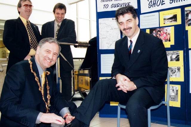 Mayor Joe Miller polishes the shoes of Derry City manager Felix Healy to support Children in Crossfire's 'Shoe Shine Week'. At back are Richard Moore (Children in Crossfire) and Des Farrell (Foyleside Shopping Centre). 1998.
