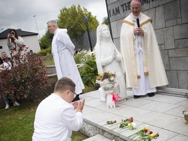 Primary 4 pupil Ollie lays his flowers at the St. Mary's Church Grotto on Thursday as Bishop Donal McKeown looks on. (Photo: Jim McCafferty Photography)