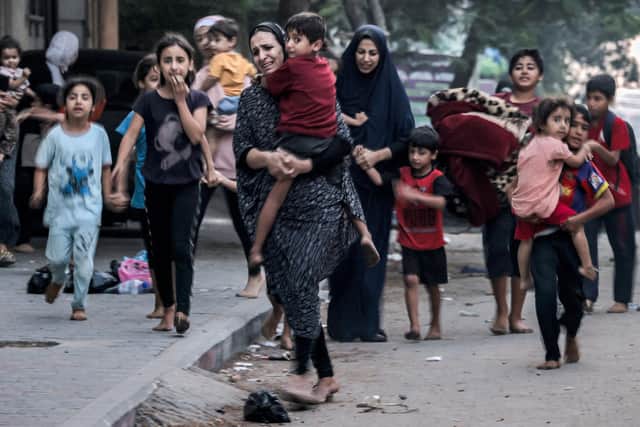 TOPSHOT - Palestinian women with their children fleeing from their homes following Israeli air strikes rush along a street in Gaza City on October 11, 2023. At least 30 people have been killed and hundreds wounded as Israel pounded the Gaza Strip with hundreds of air strikes overnight, a Hamas government official said on October 11. Israel declared war on Hamas on October 8 following a shock land, air and sea assault by the Gaza-based Islamists. (Photo by MOHAMMED ABED / AFP) (Photo by MOHAMMED ABED/AFP via Getty Images)