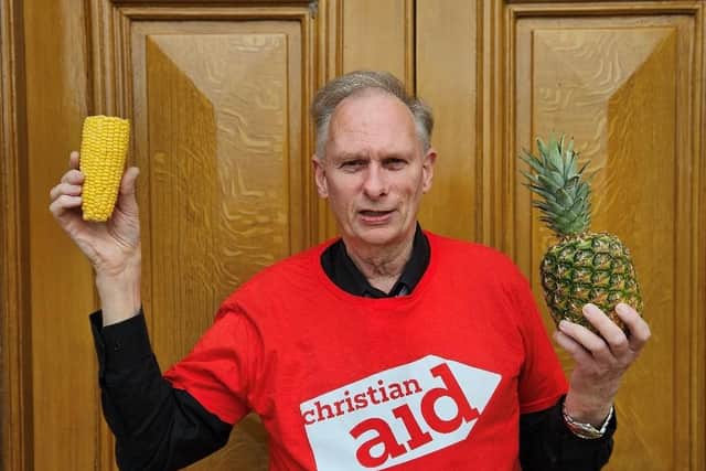 John Reid holds up a corn cob and pineapple, symbolising the work of a Christian Aid funded project which is supporting farmers in Guatemala’s ‘Dry Corridor’ to survive the climate crisis by helping corn to withstand drought and by introducing pineapple which tolerates drought well.