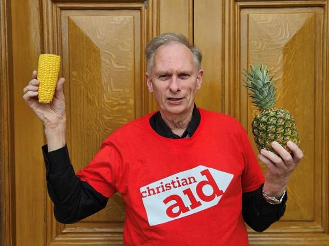 John Reid holds up a corn cob and pineapple, symbolising the work of a Christian Aid funded project which is supporting farmers in Guatemala’s ‘Dry Corridor’ to survive the climate crisis by helping corn to withstand drought and by introducing pineapple which tolerates drought well.