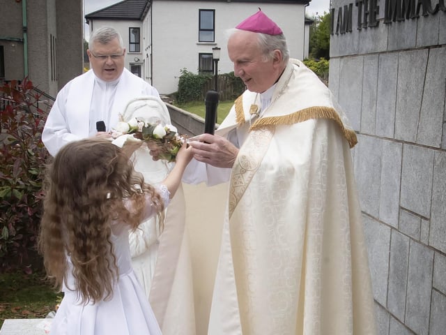 Holy Child PS pupil Matilda Condren hands over a crown of flowers for the St. Bernadette statue to Bishop Donal McKeown as Fr. McFaul looks on during Thursday's procession.