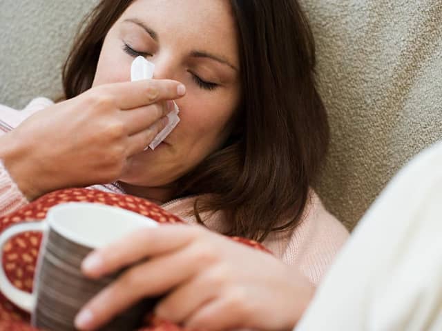 Woman with tissue and hot drink --- Image by © Royalty-Free/Corbis